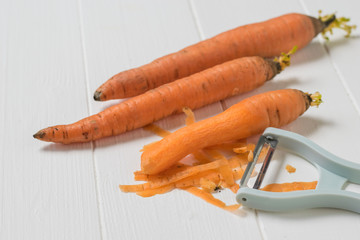Three carrots and a peeler on a white wooden table.