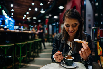 Smiling young woman eating traditional spanish churros with sugar dipped in hot chocolate sauce  in a original spanish style cafe.Happy tourist enoying traditional fried dough pastry desert in Spain.