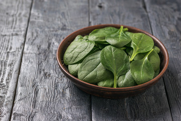 A shallow clay plate with spinach leaves on a wooden table. Food for fitness.