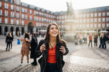 Young travel woman sightseeing urban outdoors.Traveling to Europe. Walking tour in Madrid.Backpack tourist experience.City girl.Cheerful tourist.Visiting Plaza Major square - obrazy, fototapety, plakaty