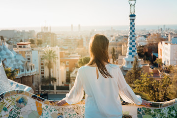 Young female tourist spending vacation in Barcelona,Catalonia,Spain.Traveling to Europe,visiting Parc Guell UNESCO site famous historical landmarks.Panoramic view on entrance.Best sunrise in Barcelona - obrazy, fototapety, plakaty
