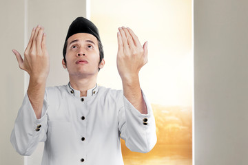 Asian Muslim man standing while raised hands and praying