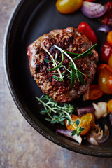 Fried hamburger steak with various cherry tomatoes and fresh herbs. Rustic background. Top view.