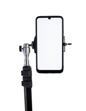 Smartphone mounted on a black tripod in a vertical position on a light isolated background tilted to the right.