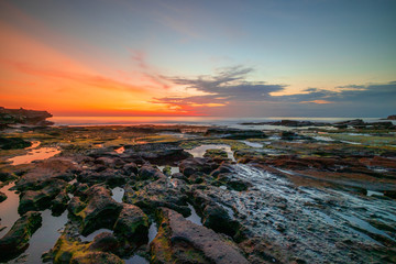 Seascape. Beach with rocks and stones. Low tide. Sun and clouds reflection in water. Slow shutter speed. Soft focus. Tanah Lot beach, Bali, Indonesia