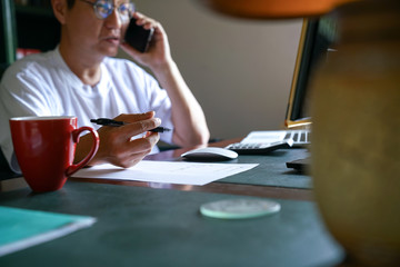 Man working from home, on his cell phone and facing his computer screen
