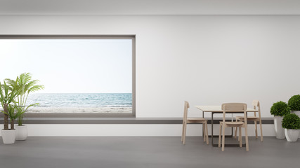 Table on concrete floor of large dining room near living area and seat in modern beach house or luxury hotel. Minimal home interior 3d rendering with sea view.