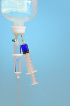 Close-up of an infusion system with an infusion containing a syringe containing blue liquid against a light blue background in medicine and space for vertical text