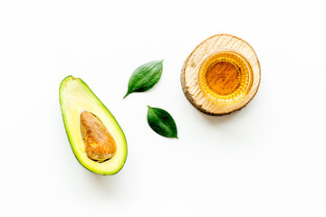 Avocado oil - for cooking - in glass bowl near halfs of vegetable on white background top-down