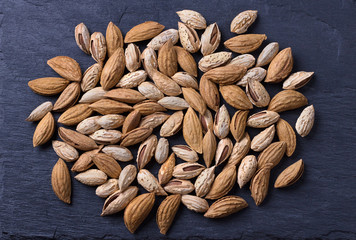 Variety of almonds, mountain and garden on black slate background. top view