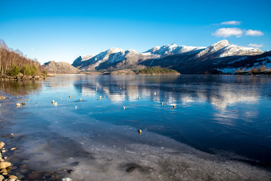 Rocks on top of ice crust of the frozen Oltedalsvatnet lake and scenic landscape of mountains, Gjesdal commune, Norway, February 2018
