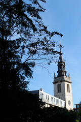 Church of St Augustine, Watling Street to the right with the tree branches as black foreground in clear blue sky, London, UK