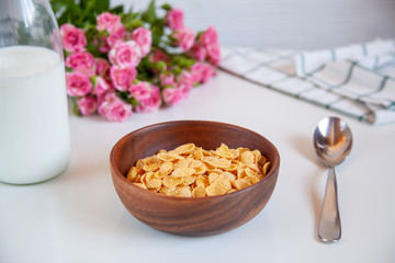 Corn flakes in a wooden plate and bottle of milk on the table.