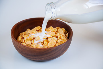 Fototapeta na wymiar Milk pouring into wooden bowl with cornflakes.
