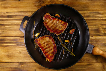 Grilled pork steaks with rosemary, garlic and spices in cast iron grill frying pan on wooden table. Top view