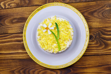Traditional russian layered salad Mimosa with spring decoration Daffodil. Decoration is made of egg, green onion and carrot. Top view