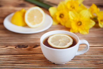 Obraz na płótnie Canvas Cap of tea with lemon and flowers on the wooden table.