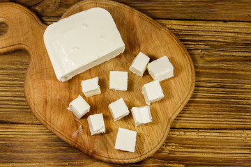 Feta cheese on cutting board on a wooden table. Top view