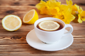 Cap of tea with lemon and flowers on the wooden table.