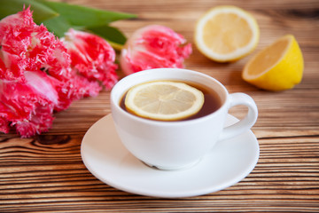 Cap of tea with lemon and flowers on the wooden table.