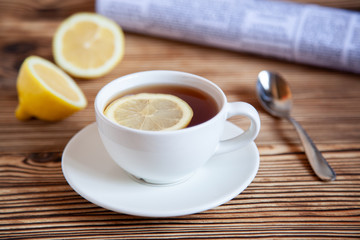 Cap of tea with lemon and paper on the wooden table.
