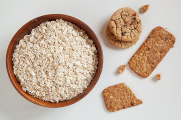 Dry oatmeal in a round wooden plate and oatmeal cookies on the table.