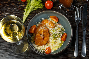 Warm Caesar salad with chicken, cheese, tomatoes and fresh herbs. White wine in a glass.