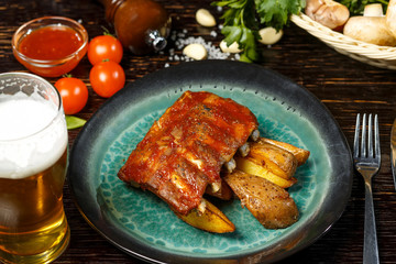 Grilled meat ribs with fried potatoes on a plate with vegetables and beer.