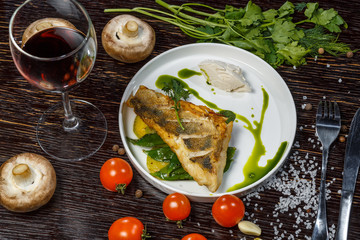 Grilled sea fish steak with cream cheese and green sauce. Glass of red wine, mushrooms, poidory and fresh herbs.