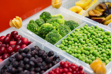 Frozen fruits and vegetables. Products are poured into plastic boxes. In the center of the frame is broccoli and green peas.