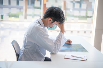 Young Asian male doctor sitting with stress headace about his work.