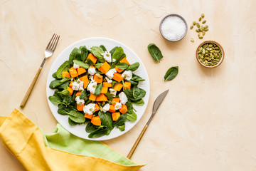 Light dish for lunch. Salad with pumpkin and basil on beige background top-down.