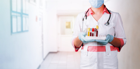 Young girl doctor in white uniform holding tray with blood tubes in her hands, standing in the hospital corridor, long banner