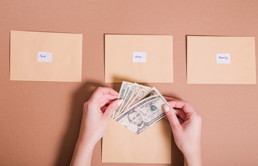 Dollars in female hands and envelopes with inscriptions for saving money on a brown background....