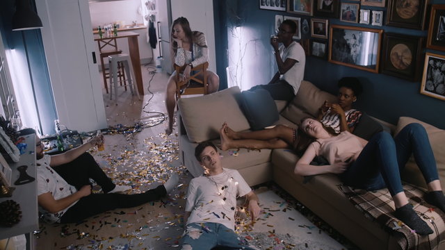 High angle sad tired friends rest, lie down exhausted after very intense party celebration in confetti covered room.