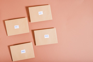 Beige envelopes with inscriptions on a brown background. Distribution of money by categories of needs