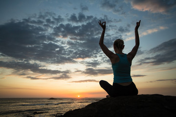 Silhouette of woman doing yoga exercises on the sea coast at twilight.