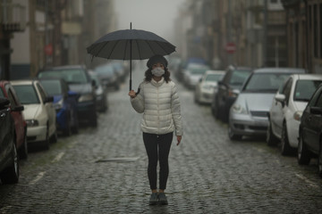 Pandemic. COVID-19, Coronovirus. A multicultural asian woman in antiviral mask stands with umbrellas in the street in cloudy weather.