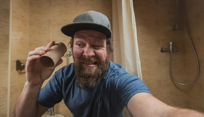 Hipster man with a distressed or disturbed face as he holds an empty roll of toilet paper in the...