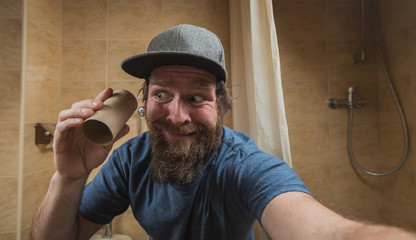 Hipster man with a distressed or disturbed face as he holds an empty roll of toilet paper in the...