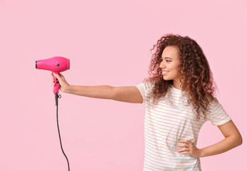 Beautiful young African-American woman with blow dryer on color background