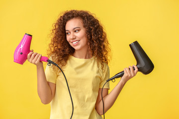 Beautiful young African-American woman with blow dryers on color background