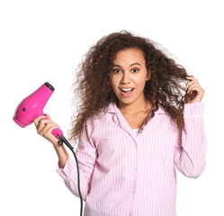 Beautiful young African-American woman with blow dryer on white background