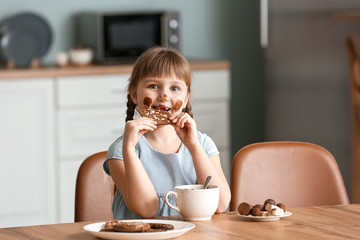 Cute little girl eating chocolate in kitchen