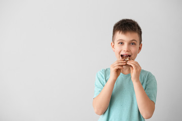 Cute little boy eating chocolate on light background