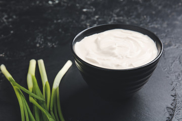 Bowl with tasty sour cream and green onion on table