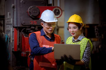 Engineer and worker industry factory wear safety uniform working and discussion detail about machine work by detail in laptop on hand control machine in factory.