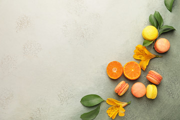 Tasty macarons with orange fruit on color background