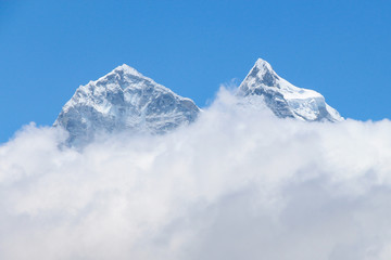 View of white snowy Kangtega mountain peak above clouds in Himalayas during the day on the way to Everest base camp in Nepal. Clear blue sky. Theme of beautiful mountain landscapes.