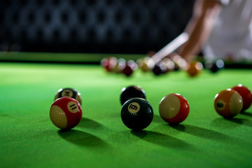Man's hand and Cue arm playing snooker game or preparing aiming to shoot pool balls on a green billiard table. Colorful snooker balls on green frieze.